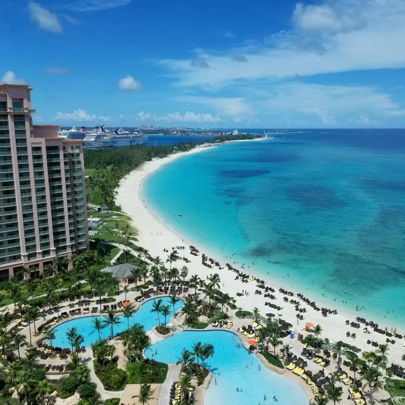 A resort located on a curved beach. The resort is a large building and has a pool.