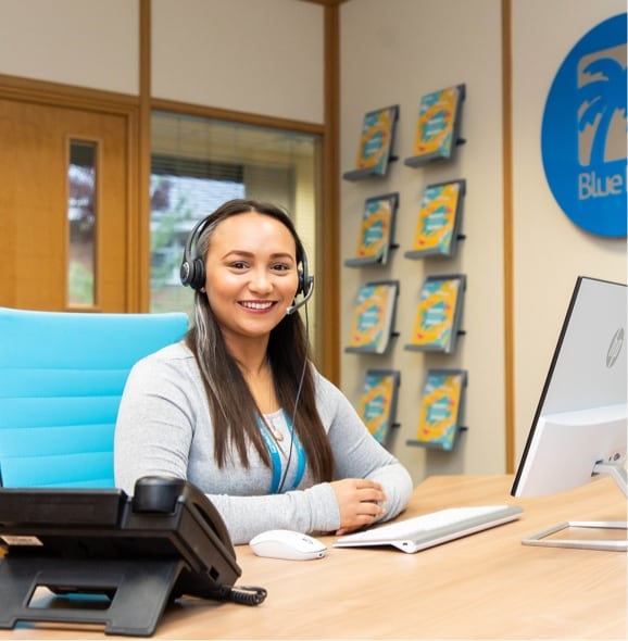 A member of customer service sits behind a desk wearing some headphones. They are looking into the camera.