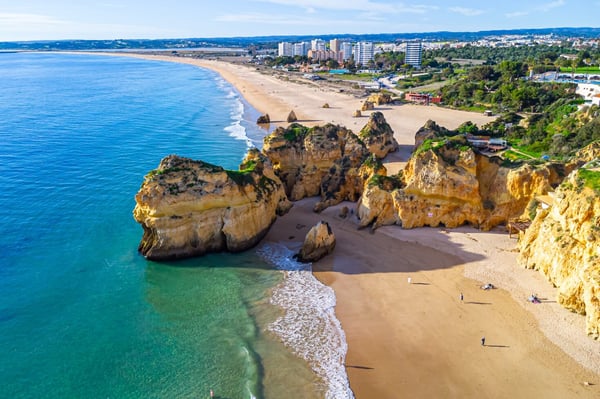 A picturesque landscape of Algarve, Portugal, featuring dramatic cliffs and a serene beach along the coastline.
