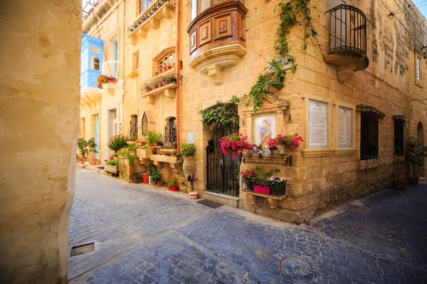 A charming narrow street in Valletta, Malta, featuring old stone buildings and a cobblestone path, typical of the historic area.