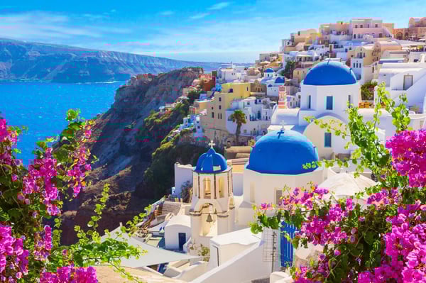 A beautiful panorama of Oia, Santorini, highlighting its famous white architecture and blue domes with a bright sky backdrop.